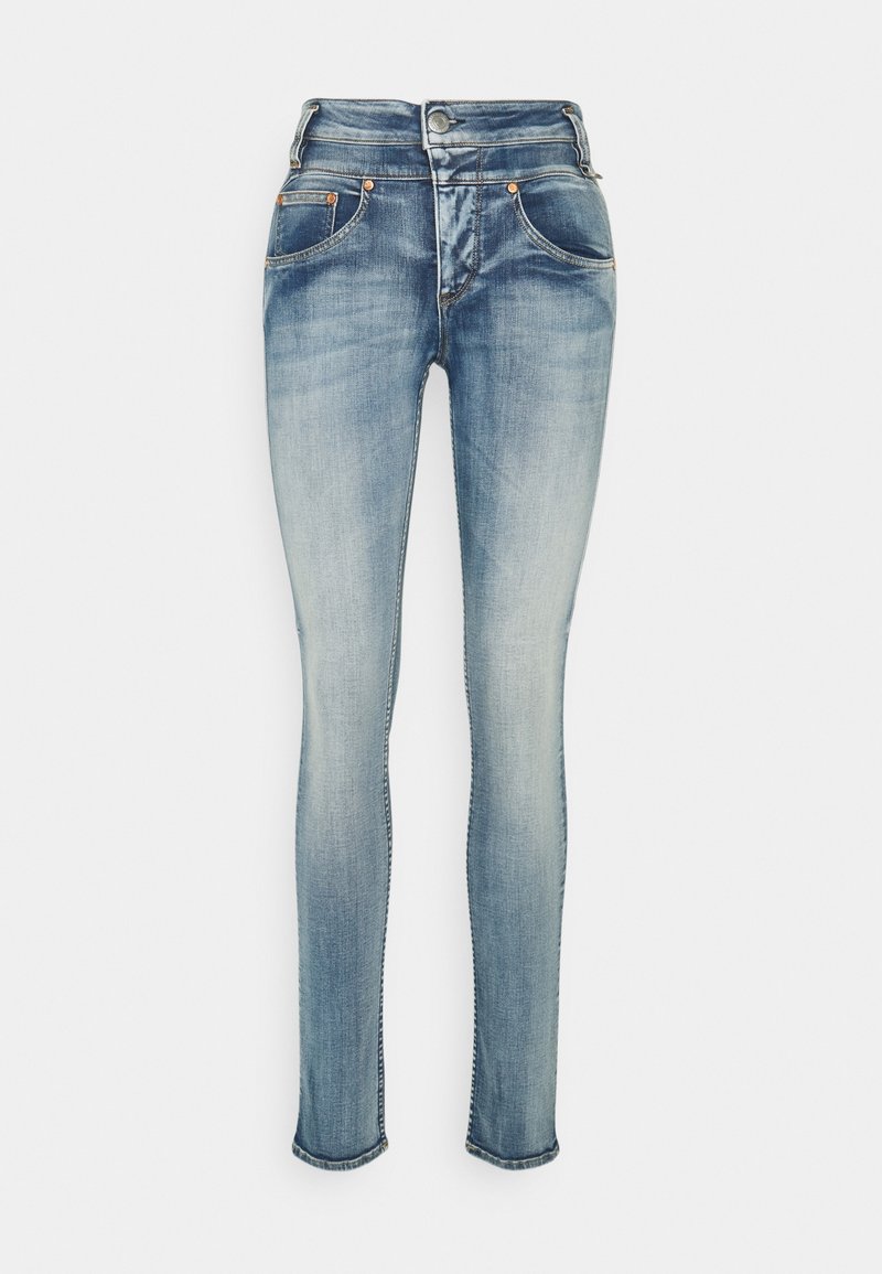 Jean skinny bleu délavé avec fermeture à boutons sur le devant et cinq poches, présenté sur fond blanc.