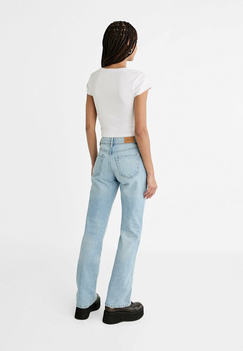 T-shirt bianca a maniche corte abbinata a jeans in denim azzurro chiaro. I jeans sono leggermente morbidi con un taglio che si allarga nel fondo. Scarpe con plateau nere.