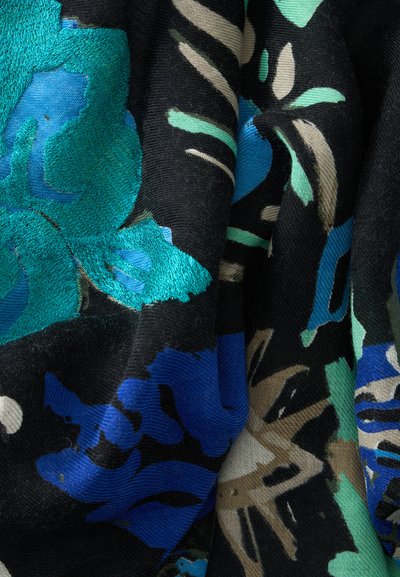 Tissu noir avec des motifs floraux abstraits bleu sarcelle, bleu, beige et vert, montrant une broderie détaillée et des plis.