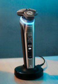 Philips Series 9000 elektrisch scheerapparaat in metallic zilver en zwart, met drie ronde scheerkoppen, LCD-display en basis oplaadstation.