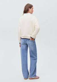 White sweater with a high collar, navy trim; loose-fitting light blue jeans; pink slip-on shoes; smooth fabric and casual style.