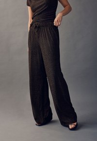 Černé kalhoty s širokými nohavicemi a lesklou texturou, s elastickým pasem a stahovací šňůrkou. Styly s černými páskovými lodičkami.