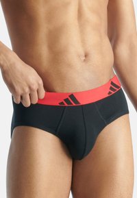 Svarta kalsonger med ett rött elastiskt midjeband som har svart logotyp. Slätt tyg med en nära passform, lämpliga för vardagsbruk.