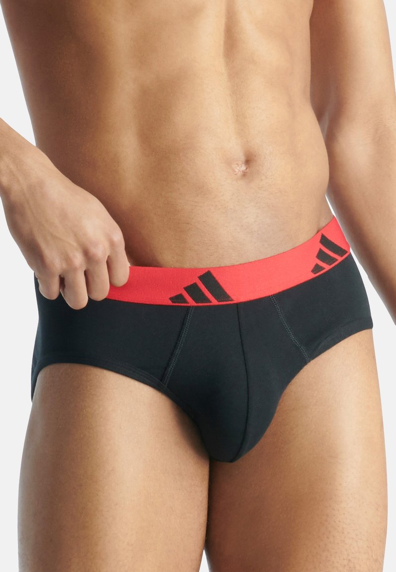 Slip neri con elastico rosso in vita e branding nero. Tessuto liscio con vestibilità aderente, adatto per l'uso quotidiano.