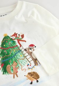 Sweatshirt couleur crème avec des animaux brodés décorant un arbre de Noël avec des lumières et des ornements colorés. Encolure ronde et texture douce.