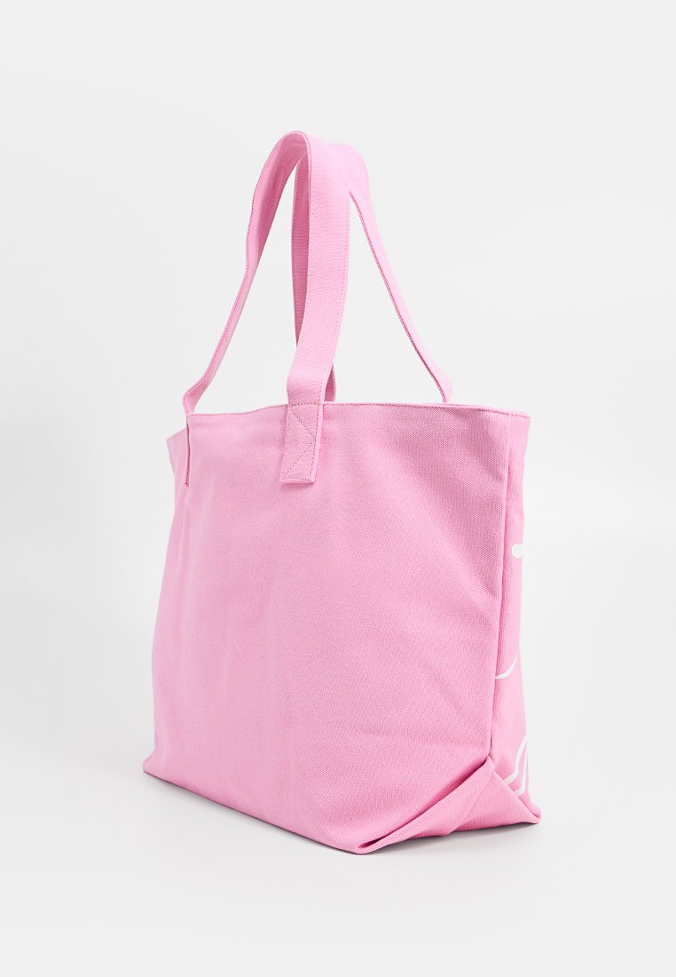 Sac fourre-tout en tissu rose avec deux larges poignées, se tenant debout contre un fond blanc uni.