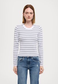 Maglietta bianca a maniche lunghe con strisce orizzontali grigie, caratterizzata da un colletto a girocollo e texture a coste, abbinata a jeans blu strappati.