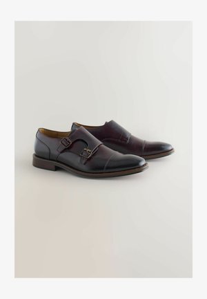 Tumed pruunid nahkkingad, millel on elegantne disain. Omavad kaht kinnitust ja siledat tekstuuri, ümarat ninaosa ning kontrastset õmbluse detaili.