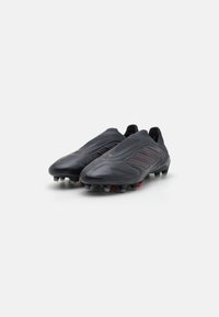 Schwarze Fußballschuhe mit schlankem Design, ausgestattet mit roten Akzenten und einer strukturierten Oberseite. Genopptes Außensohlenprofil für Halt auf Rasenflächen.