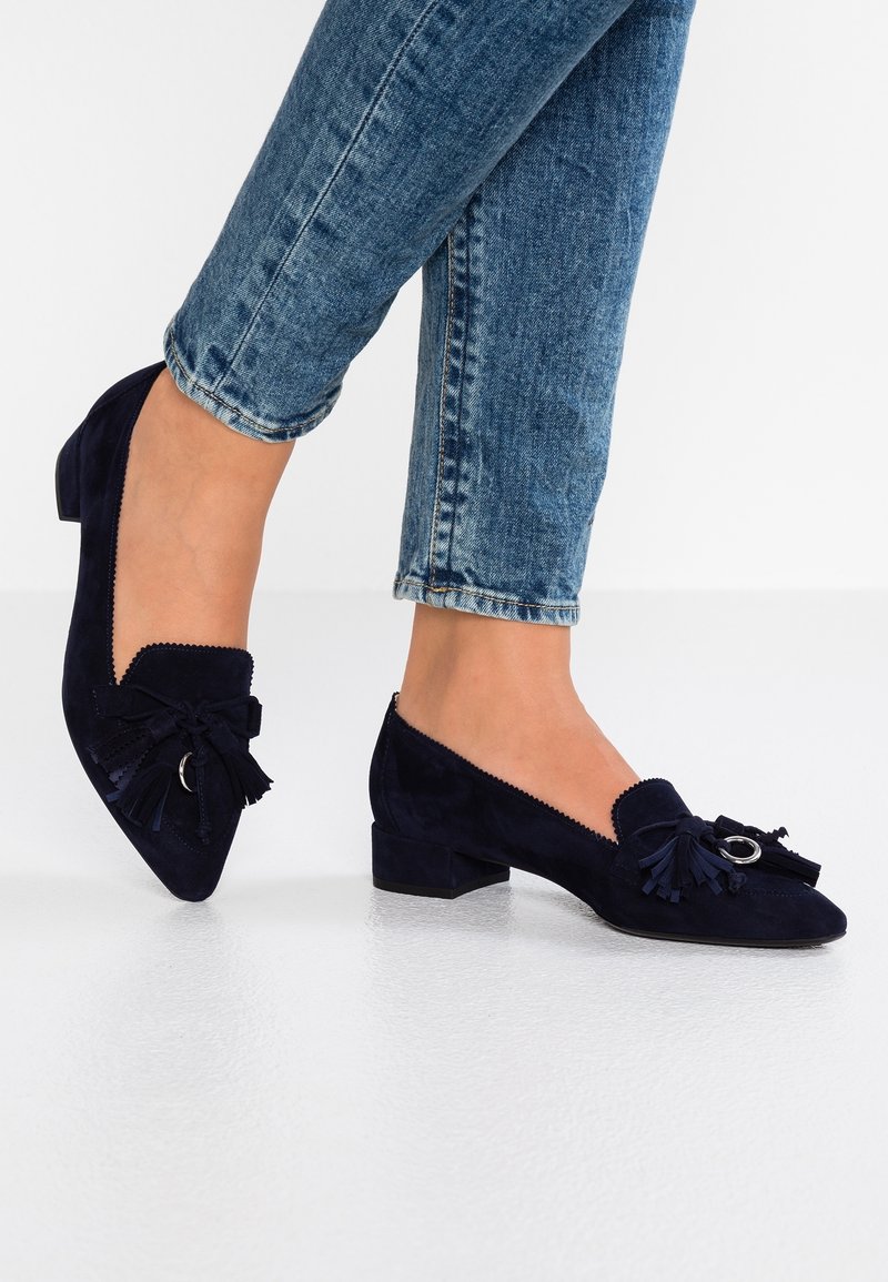 Marineblauwe suède lage hakken met een spitse neus, met decoratieve franjes en een cirkelvormige accent aan de voorkant.