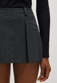 Donkergrijze geplooide rok van gestructureerde stof, voorzien van een riemlus en een zijzak. Boven de knie gesneden voor een gestructureerde pasvorm.