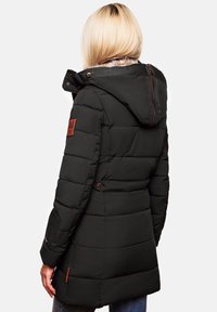 Black puffer jacket with a fur-lined hood, featuring stitched panels, brown button accents, and a patch on the left sleeve.