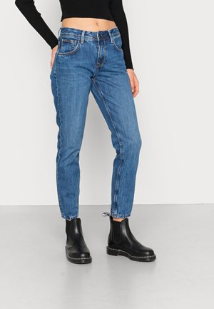 Jeans de denim azul claro com corte reto, apresentando dois bolsos laterais e uma bainha crua. Combinados com botas Chelsea pretas.