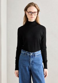 Svart polotröja i kombination med högmidjade blå denimjeans. Tröjan har åtsittande ärmar; jeansen har knäppning och en lätt tvätt.