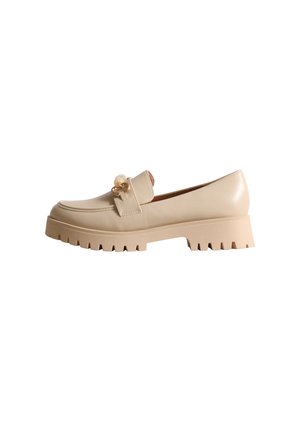 Mocassin en cuir beige avec un ornement doré et une semelle épaisse à crampons profonds, présenté de profil sur fond blanc.