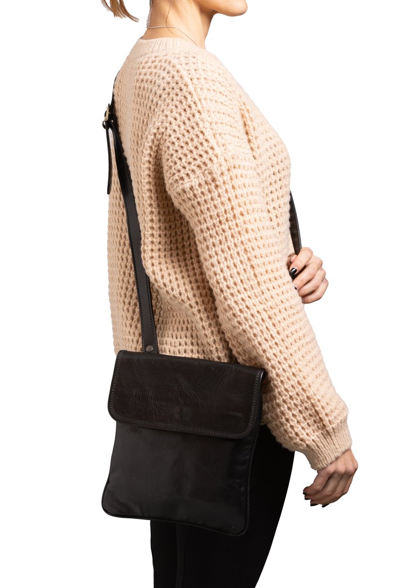 Borsa a tracolla nera in pelle con design piatto, texture liscia e chiusura a patta; indossata su un maglione beige con texture.
