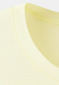 Gros plan sur l'encolure d'un T-shirt en coton jaune pâle avec des coutures visibles et une texture de tissu douce.