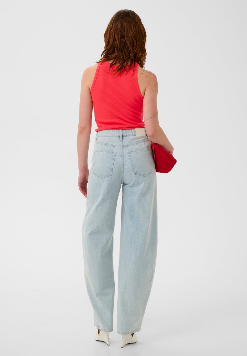 Red tank top paired with light blue, high-waisted, wide-leg jeans. The model holds a red clutch. White heeled shoes are visible.