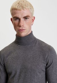 Maglione grigio a collo alto realizzato in morbido tessuto a maglia, con un colletto a coste alto e un design attillato, caratterizzato da una texture liscia e un minimo di dettagli.