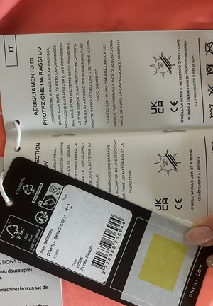 Labels voor O'Neill-kleding met informatie over UV-bescherming in het Italiaans en Frans, maat 12, kleur funky perzik en wasvoorschriften.