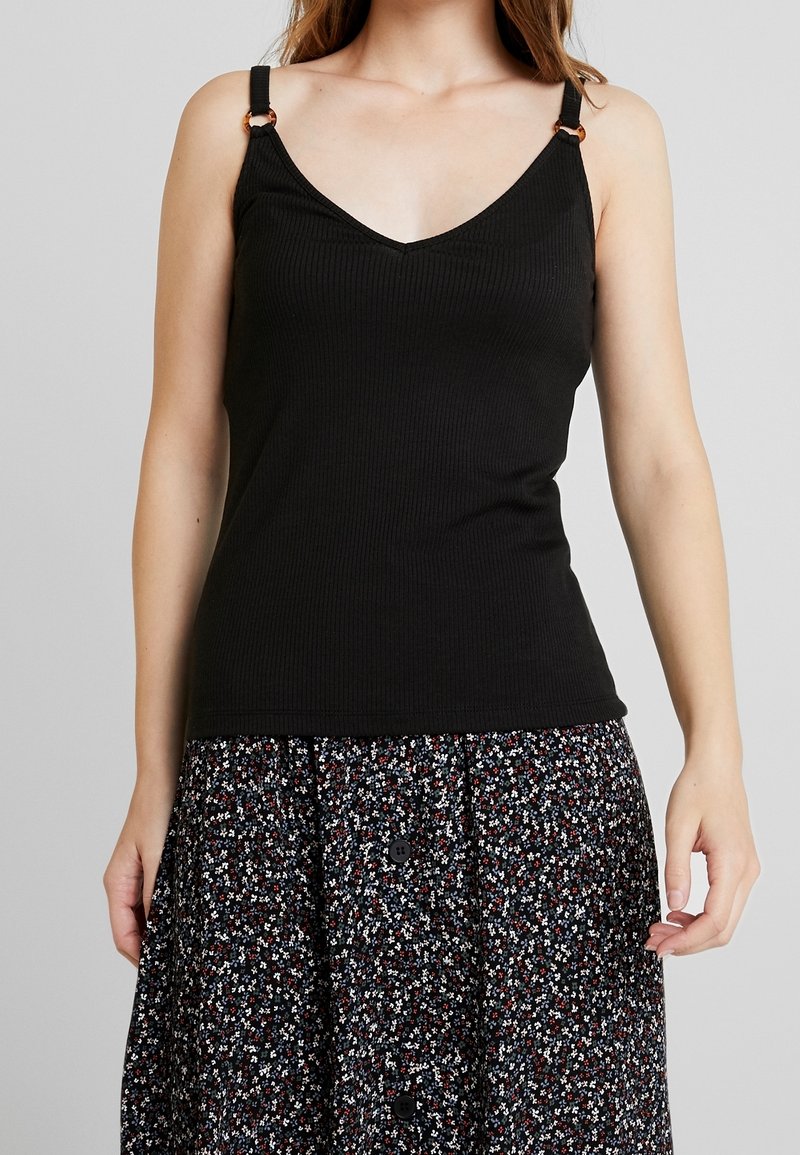 Černý proužkovaný top na ramínka s výstřihem do V, s nastavitelnými ramínky zdobenými zlatými doplňky. V kombinaci s sukní s květinovým vzorem.
