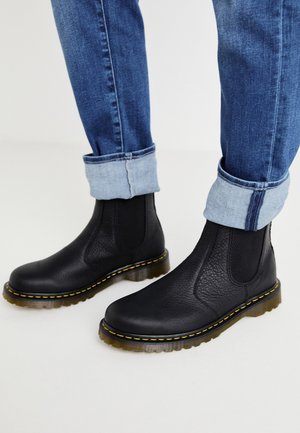 Sorte læder Chelsea-støvler med elastiske sider og en struktureret overdel. Har gule syninger og en gennemsigtig, kraftig sål.