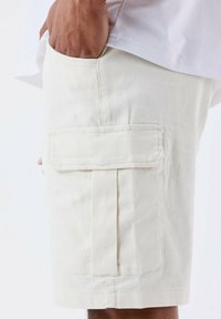 Bermudas cargo beige con un gran bolsillo lateral, hechas de una tela resistente con un acabado texturizado y un diseño recto.