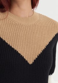 Sweter dziergany z motywem kolorystycznym w beżowym, czarnym i kremowym kolorze. Wyraźne teksturowane wzory z prążkowanym, okrągłym dekoltem.