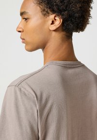 Koszulka krótki rękaw w kolorze taupe wykonana z miękkiego materiału. Posiada proste przeszycia na ramionach oraz klasyczny dekolt typu crew neck.