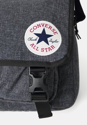 Borsa a tracolla in tessuto grigio con una superficie liscia, con una toppa rotonda con "Converse All Star" e un design a stella, e una chiusura con fibbia in plastica.