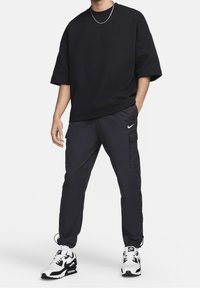 Černá oversized košile s jemnou texturou loga Nike, spárovaná s tmavými cargo kalhotami s bočními kapsami. Obuv tvoří bílo-černé tenisky.