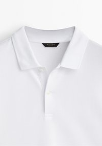 Polo blanc en tissu texturé, avec un col classique, une patte de boutonnage à deux boutons et une petite étiquette de marque au niveau du col.