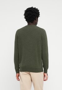 Pull en maille vert foncé avec des manches longues, un col rond et une coupe décontractée. Texture lisse avec un motif chiné subtil.