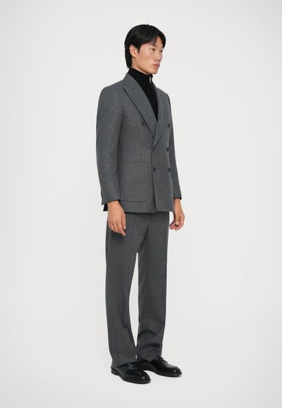 Hallide kahekordne ülikond, millel on vertikaalsed triibud, slim fit, nurgelised krae ja must polo kaeluses. Mustad kingad täiustavad välimust.