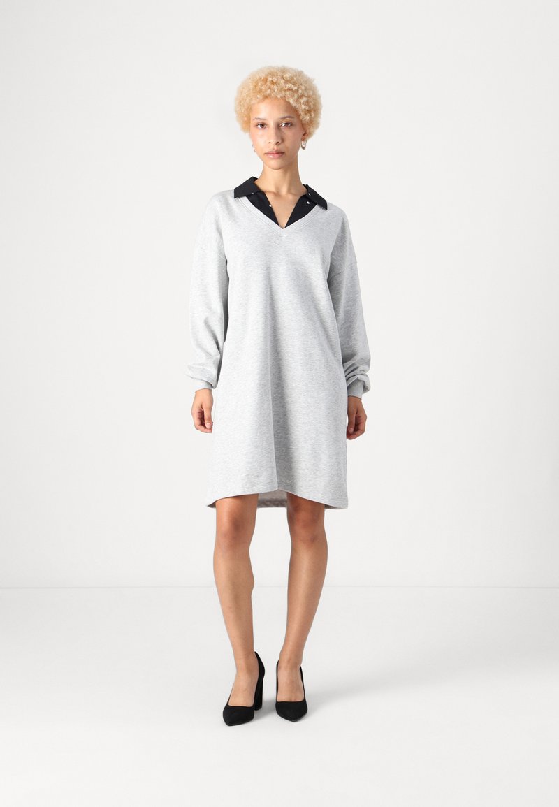 Vestido de moletom cinza com decote preto, mangas longas e bainha ligeiramente curva, combinado com sapatos de salto alto pretos.