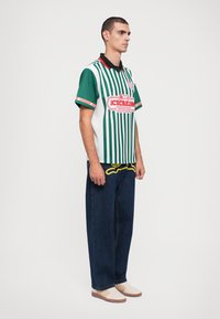 Groen en wit gestreept shirt met een zwarte kraag, met de tekst "ICECREAM SUPPLIES" in het rood. Gemaakt met blauwe spijkerbroek en beige schoenen.