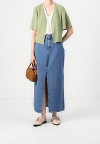 Světle zelená zkrácená bunda, bílý tričko s výstřihem do V, denimová maxi sukně s předním rozparkem, hnědá tkaná kabelka, béžové mokasíny s přezkami.