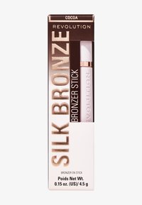 Bronzer-stift i färgen kakao, förpackad i en vit och guld box med texturerade mönster och en tydlig produktetikett. Nettovikt 4,5 g.