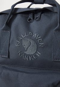 Mörkblå Fjällräven Kånken-ryggsäck med en cirkulär logotyp, dubbla dragkedjor och en texturerad tyfinish. Accenter i en något ljusare blå.