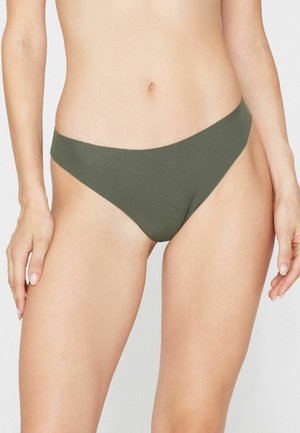 Kobieta nosząca oliwkowo zielone dół bikini, pokazująca środkową część ciała i górną część nóg na jednolitym jasnym tle.