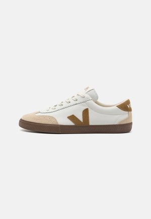 White sneakers with tan suede accents, featuring a textured brown rubber sole, lace-up closure, and a logo on the heel.