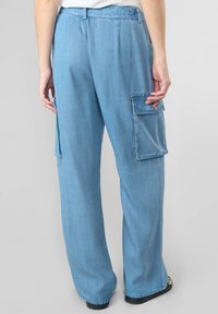 Pantaloni cargo in denim blu chiaro con gambe larghe, dotati di tasche laterali e una vestibilità comoda. La texture del tessuto appare morbida con leggeri effetto sbiadito.