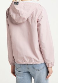 Veste rose clair avec capuche, poignets élastiques et ourlet à cordon de serrage. Faite en tissu lisse, avec une étiquette au dos du col.