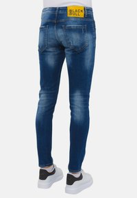 Heren blauwe denim jeans met een slim fit, voorzien van een gele logopatch op de tailleband en subtiele wassing op de benen.
