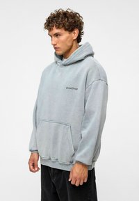 Lichtgrijze oversized hoodie gemaakt van een zachte katoenmix. Heeft een kangoeroezak en een geborduurd "Create Change" logo op de borst.