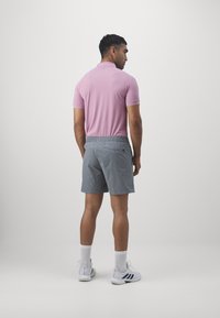 Polo de color rosa claro, con mangas cortas y cuello, combinado con pantalones cortos grises con cintura elástica y bolsillo trasero. Zapatillas blancas y calcetines.