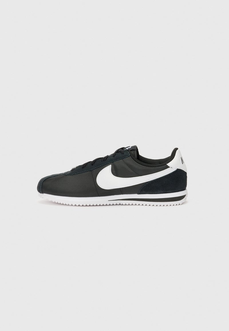 Crna atletska cipela s bijelim Nike logotipom, gornji dio od velura i sintetičkog materijala, dizajn s vezicama i strukturirana gumena potplat. Bočni prikaz.