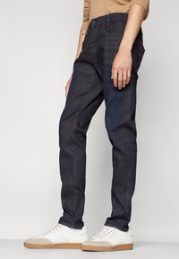 Jeans in denim scuro con una vestibilità slim, caratterizzati da un classico design a cinque tasche, sottili dettagli di cucitura e lievemente usurati nelle ginocchia.
