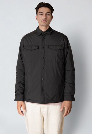 Musta pikeetakki kauluksella, jossa kaksi rintataskua ja teksturoidut hihat. Kangas on sileää ja keskivahvaa.