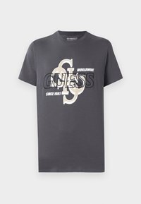 Szary bawełnowy t-shirt z krótkim rękawem z dużym nadrukiem graficznym w czerni i beżu, zawierającym teksty "GUESS", "WORLDWIDE" oraz "SINCE 1981."